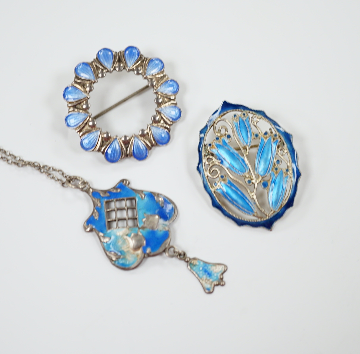 A George V silver and enamel set drop pendant (a.f.), 40mm on a white metal chain and two white metal and enamel brooches, one stamped sterling.